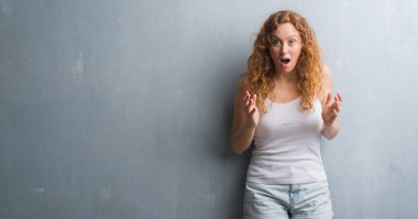 Gri grunge duvar bir sürpriz yüz, korkuyor ve heyecanlı korku ifadesi ile şok korkmuş genç Kızıl saçlı kadın