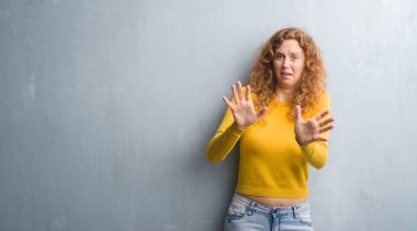 Şokta bağırarak gri grunge duvar korkuyor ve dehşet korku ifade dur hareketi el ile ile genç Kızıl saçlı kadın. Panik kavramı.