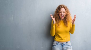 Kızgın ve silah ile başarı için deli duvar gri grunge kutluyor üzerinde genç Kızıl saçlı kadın kaldırdı ve heyecanlı çığlık gözler kapalı. Kazanan kavramı