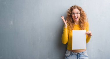 Gri grunge genç Kızıl saçlı kadın duvar büyük gülümseme ile çığlık zaferini kutluyor ve ellerini kaldırdı boş kağıt sayfası çok mutlu ve heyecanlı, kazanan ifade holding