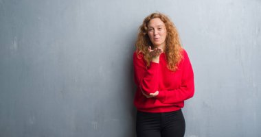 Genç redhead gri grunge duvar giyen üzerinde kırmızı kadın kazak bir öpücük el ile güzel ve seksi olmak hava üfleme kamera bakıyor. Aşk ifade.