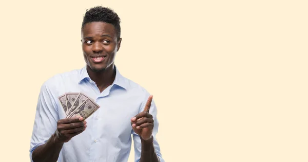 幸せそうな顔 ナンバーワンのアイデアや質問ポインティング指でドルを保有若いアフリカ系アメリカ人のビジネスマンを驚かせた — ストック写真