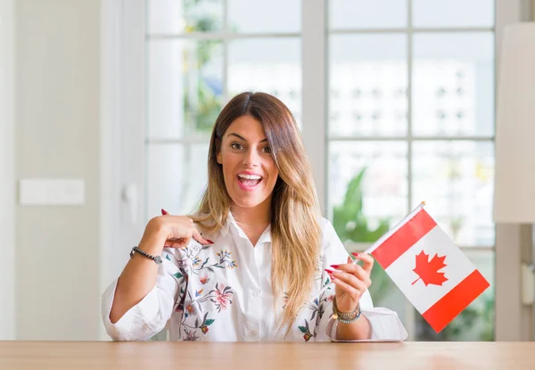 年轻女子在家里持有加拿大国旗与惊讶的脸指向自己的手指 — 图库照片