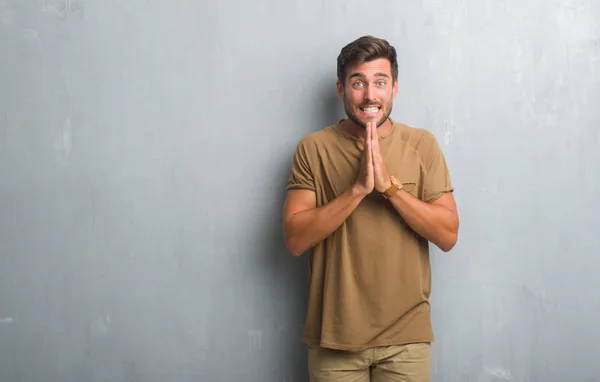 Guapo Joven Sobre Gris Pared Grunge Orando Con Las Manos — Foto de Stock