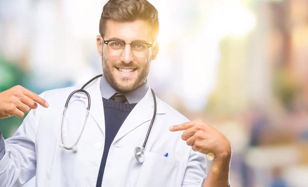 若いハンサムな医者の顔に笑顔と自信を持って 誇りと幸せな指で自分を指している孤立した背景の上の男 — ストック写真