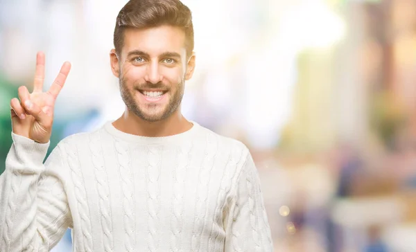 若いハンサムな男で冬のセーターを着て分離を示す背景と自信を持って 幸せな笑みを浮かべている間 つ番号を指で上向き — ストック写真