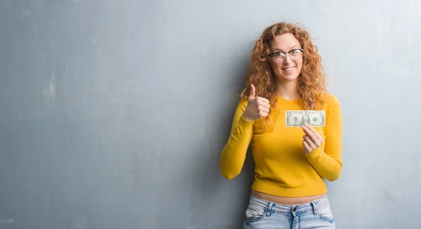 Mulher Ruiva Jovem Sobre Parede Grunge Cinza Segurando Dólar Feliz — Fotografia de Stock