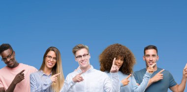 Grup gülümseyen ve iki ile işaret kamera bakarak mavi blackground üzerinde arkadaşıyla bileşimi eller ve yan parmak.