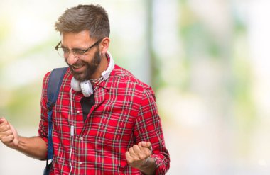 Üzerinde kulaklık ve sırt çantası giyiyor yetişkin İspanyol öğrenci adam arka plan çok mutlu ve heyecanlı kaldırdı, silah ile kazanan jest yapıyor gülümseyen ve başarı için çığlık izole. Kutlama kavramı.