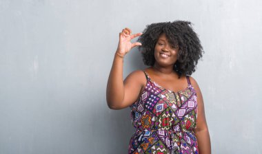 Renkli elbise gülümseyen ve süre seyir ve kamera boyutu işaret parmaklarıyla yapıyor el ile kendinden emin eller gri grunge duvarın üzerinden genç Afro-Amerikan kadın. Ölçü kavramı.