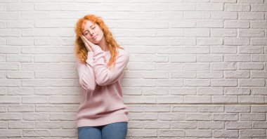 Uyku yorgun hayal ve eller ile birlikte kapalı gözlerle gülümseyerek poz tuğla duvarın üzerinden duran genç Kızıl saçlı kadın.