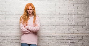 Tuğla duvar şüpheci ve gergin duran, çapraz kolları olan yüzündeki ifade onaylamayan genç Kızıl saçlı kadın. Negatif kişi.