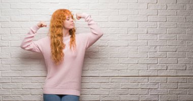 Gururlu gülümseyen kol kasları gösterilen tuğla duvar üzerinde duran genç Kızıl saçlı kadın. Fitness kavramı.