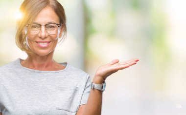 Neşeli sunulması ve kameraya bakarak avucunun ile işaret gülümseyen izole arka plan üzerinde gözlük takan orta yaş İspanyol kadın kıdemli.