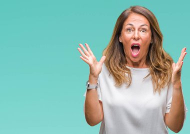 Orta yaş üst düzey İspanyol kadın deli kutluyor arka plan izole ve başarı için kaldırdı kollarını açarak hayrete ve heyecanlı çığlık gözleri açık. Kazanan kavramı