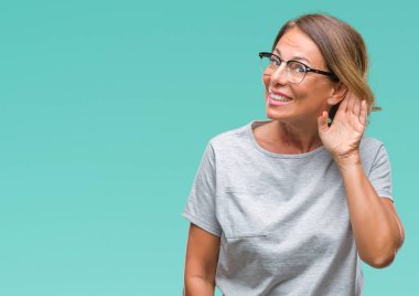 Middle age senior hispanic woman wearing glasses over isolated background smiling with hand over ear listening an hearing to rumor or gossip. Deafness concept. clipart