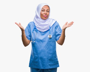 Orta yaş üst düzey Arap izole arka plan clueless ve şaşkın bir ifadeyle kollar ve eller kaldırdı üzerinde hijab giyen kadın hemşire. Şüphe kavramı.