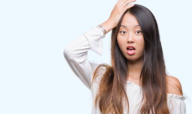 Young asian woman over isolated background surprised with hand on head for mistake, remember error. Forgot, bad memory concept. clipart