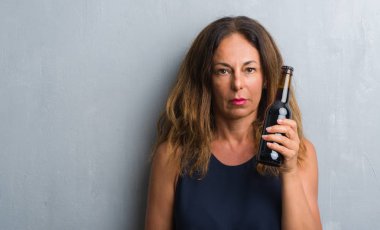 Acımak yüz ciddi düşünüyorum üstünde kendine güvenen bir ifade ile bira şişesi holding gri grunge duvarın üzerinden duran orta yaş İspanyol kadın