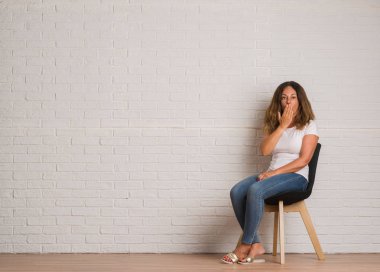 Orta yaş İspanyol kadın beyaz tuğla walll kapak ağız için hata, ifade korku, utanç ile şok el ile üzerinden sandalyede oturan sessizlik içinde gizli kavramı korkuttu