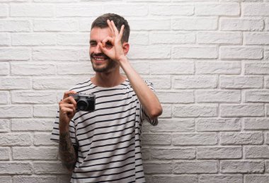 Mutlu yüz el parmaklarının arasından seyir göz üzerinde ok işaretiyle yapıyor gülümseyen ile beyaz tuğla duvarın üzerinden vintage fotoğraf makinesi ayakta tutan genç adam