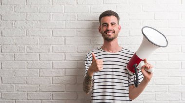 Ok işareti, başparmak ile parmak, mükemmel işareti yapıyor kocaman bir gülümseme ile megafon mutlu tutan genç yetişkin adam