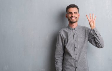 Gösterilen ve parmakları ile işaret gri grunge duvarın üzerinden duran genç yetişkin adam sırasında kendinden emin ve mutlu gülümseyerek dört numara.