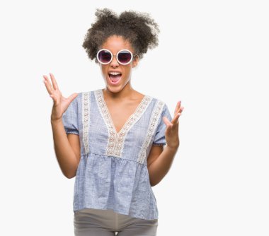 Kızgın ve çığlık kaldırdı ve kapalı gözleri heyecanlı silah ile başarı için deli kutluyor izole arka plan üzerinde gözlük takan genç afro Amerikalı kadın. Kazanan kavramı