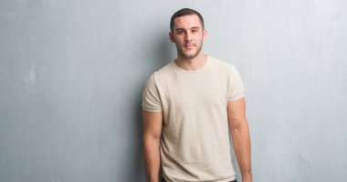 Genç beyaz adam akıllı yüzünde ciddi düşünme emin bir ifade ile gri grunge duvarın üzerinden