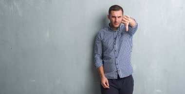 Beyaz delikanlı mutsuz ve kızgın ret gösterilen ve başparmak aşağı hareketi ile negatif seyir gri grunge duvarın üzerinden. Kötü ifade.