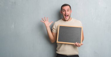 Blackboard çok mutlu ve heyecanlı, kazanan ifade ile çığlık zaferini kutluyor büyük holding gri grunge duvarın üzerinden beyaz delikanlı gülümse ve el kaldırdı