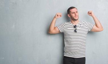 Beyaz genç gururlu gülümseyen kol kasları gösterilen gri grunge duvarın üzerinden. Fitness kavramı.