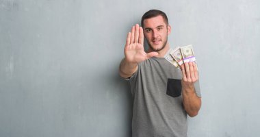 Genç beyaz adam açık eliyle dur işareti ile ciddi ve kendine güvenen ifade, savunma jest yapıyor para tutan gri grunge duvarın üzerinden