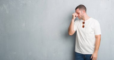 Beyaz genç güneş gözlüğü yorgun sürtünme burun ve göz yorgunluğu ve baş ağrısı duygu gri grunge duvarın üzerinden. Stres ve hayal kırıklığı kavramı.