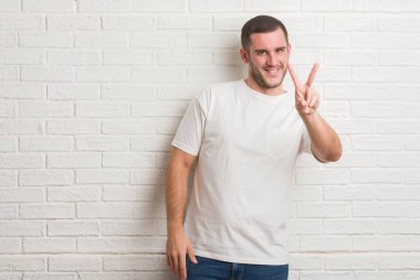 Zafer işareti yapıyor parmak gösterilen kamera seyir gülümseyen beyaz tuğla duvarın üzerinden ayakta beyaz delikanlı. İki numaralı.