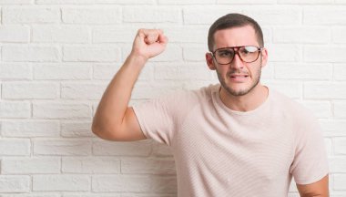 Genç beyaz adam ayakta üzerinde beyaz tuğla duvar giyen gözlük rahatsız ve hayal kırıklığına uğramış bağırarak öfkeyle, çılgın ve bağrışmalar yükseltilmiş el, öfke kavramı ile