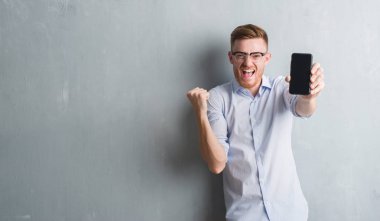 Duygu tezahürat genç Kızıl saçlı adam gri grunge duvar gösteren boş ekran gurur çığlık ve zafer ve başarı çok heyecanlı, kutluyor Smartphone