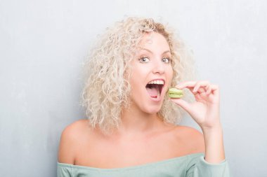 Sarışın genç kadın macaron acımak yüz ciddi düşünüyorum üstünde kendine güvenen bir ifade ile yemek grunge gri arka plan üzerinde