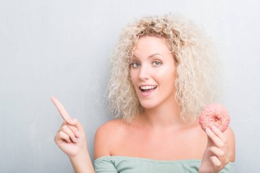 Sarışın genç kadın grunge üzerinde gri pembe çörek el ve parmak ile tarafına işaret çok mutlu yemek arka plan