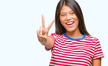 Genç Asyalı kadın mutlu yüz zafer işareti yaparken kameraya göz kırpıyor ile gülümseyen izole arka plan üzerinde. İki numaralı.