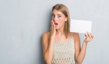 Hata, korku, sessizlik içinde gizli kavramı korkmuş ifade için utanç ile boş kartı kapak ağız eliyle tutarak grunge gri duvar güzel genç kadın şok