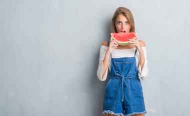 Güzel genç kadın ciddi düşünme akıllı yüzünde kendinden emin bir ifade ile karpuz yeme grunge gri duvarın üzerinden