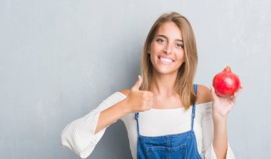 Güzel genç kadın nar ile mutlu büyük holding grunge gri duvar yüzünden gülümseme ok işareti, başparmak ile parmak, mükemmel işareti yapıyor