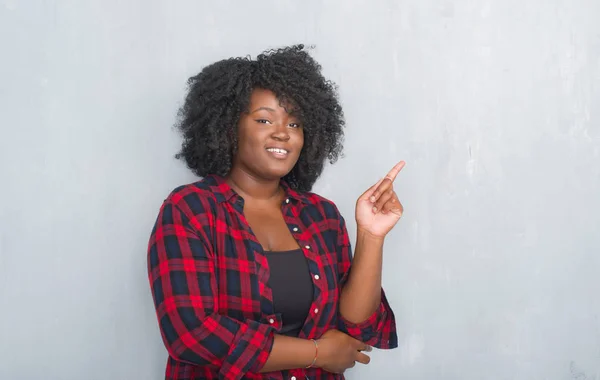 年轻的非洲裔美国人时髦的女人在灰色的垃圾墙上 脸上带着微笑 用手和手指指着侧面看着相机 — 图库照片