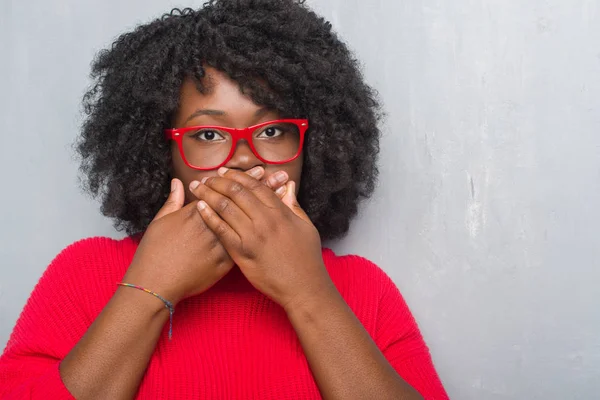 Genç Afro-Amerikan artı boyutu kadın ağız hata için elleriyle kapsayan şok kış kazak giyen gri grunge duvarın üzerinden. Gizli kavramı.