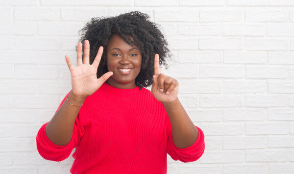 Молодой африканский американец плюс размер женщины над белой кирпичной стеной показывая и показывая пальцами номер шесть улыбаясь уверенно и счастливо
.