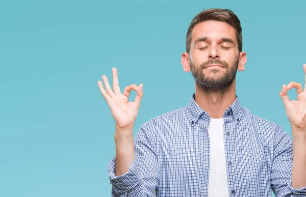 İzole arka plan üzerinde beyaz t-shirt giyen genç yakışıklı adam rahatla ve gülümseyen gözlerle kapalı parmak jestle meditasyon yapıyor. Yoga kavramı.