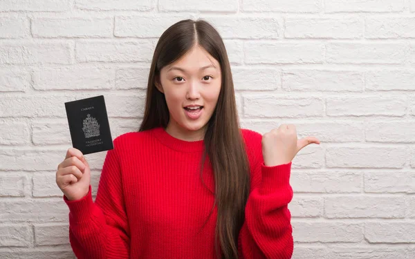 Joven Mujer China Sobre Muro Ladrillo Sosteniendo Pasaporte Canadá Señalando —  Fotos de Stock
