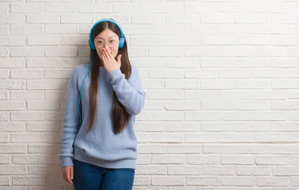Mladá Číňanka Cihlová Zeď Nošení Sluchátek Kryt Ústa Rukou Šokován — Stock fotografie