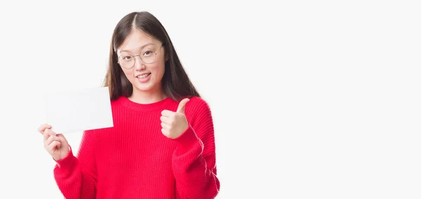 年轻的中国妇女在孤立的背景持有空白卡高兴的大笑做 拇指与手指 优秀的标志 — 图库照片
